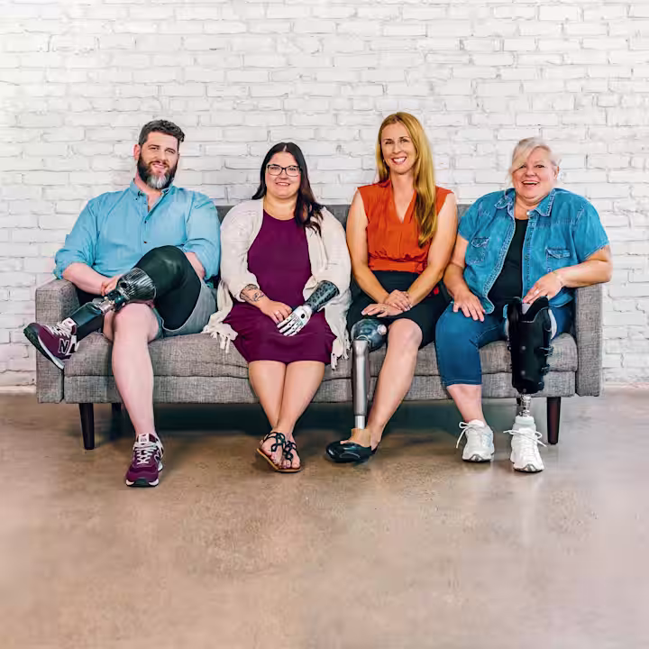 Quattro persone sedute su una panchina. Un uomo con una protesi alla gamba sotto il ginocchio, una donna con una mano bionica, una donna con una protesi al ginocchio C-Leg e una donna con una protesi transtibiale.