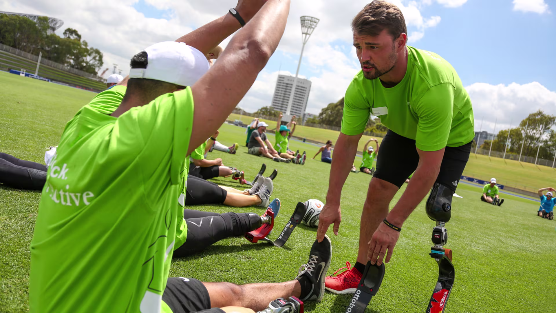 Running coach and former Paralympian Heinrich Popow helps an amputee athlete stretch their legs in an outdoor field