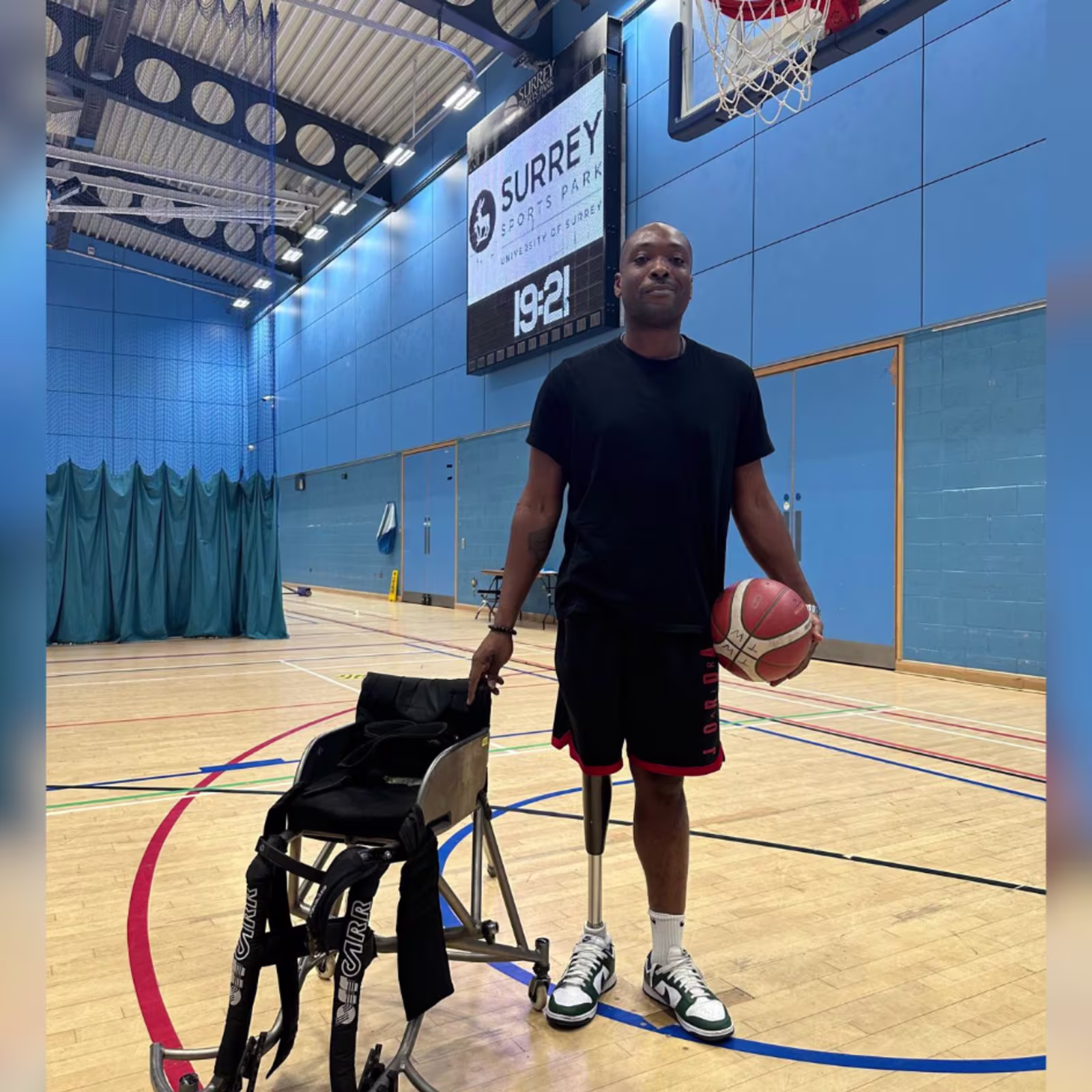 C-Leg user Vickson stands on a basket ball court with an orange basketball under one arm and holding onto his wheelchair for basketball in the other.