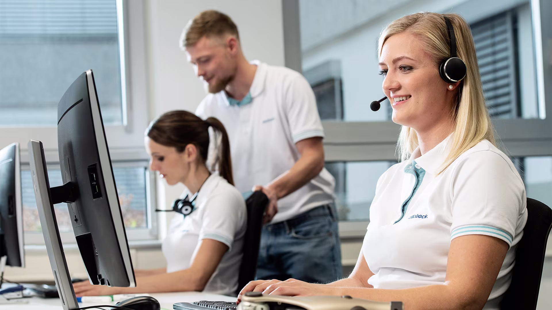Ottobock customer support team collaborating in modern office with headsets and computers.