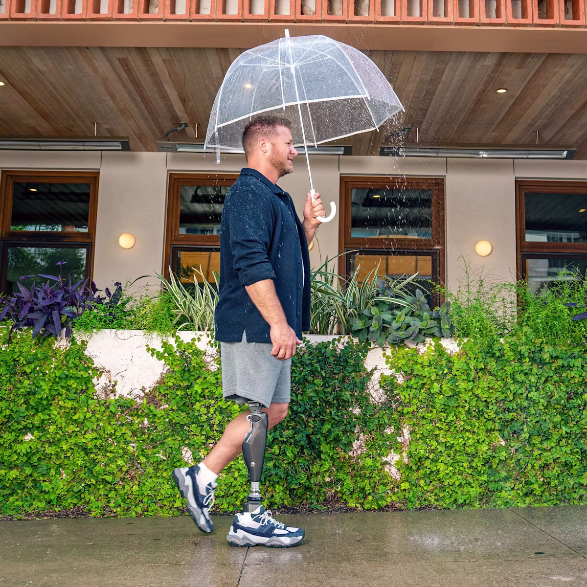 A man with a C-Leg prosthetic knee from Ottobock walking in the rain holding an umbrella.