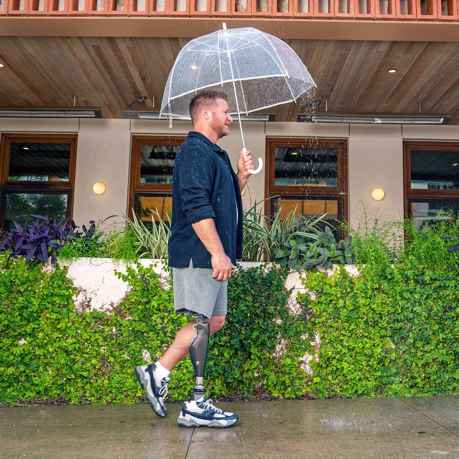 A man with a C-Leg prosthetic knee from Ottobock walking in the rain holding an umbrella.