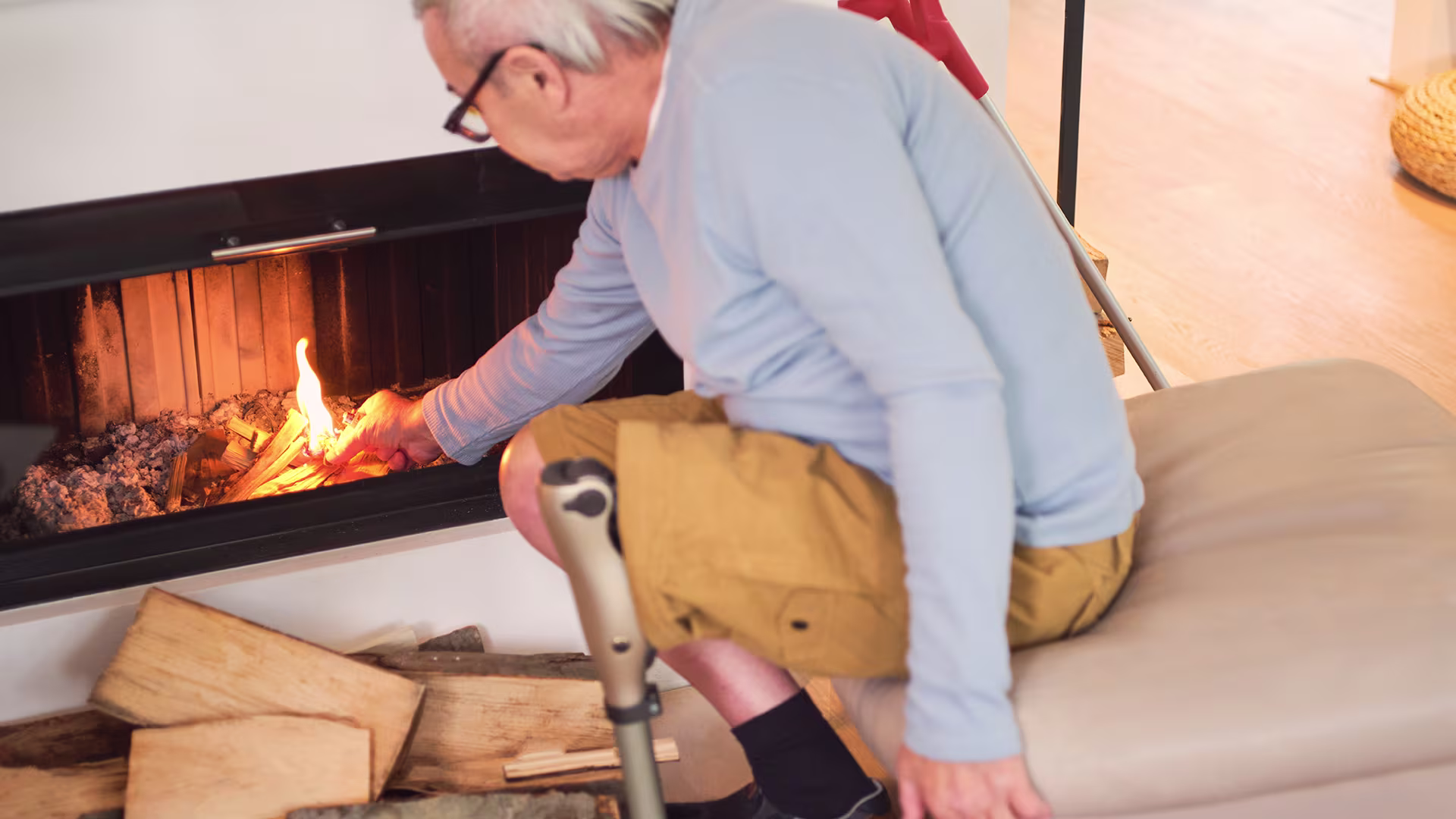 Ein älterer Herr, der die Kenevo Kniegelenksprothese von Ottobock trägt, zündet ein Feuer im Kamin an.