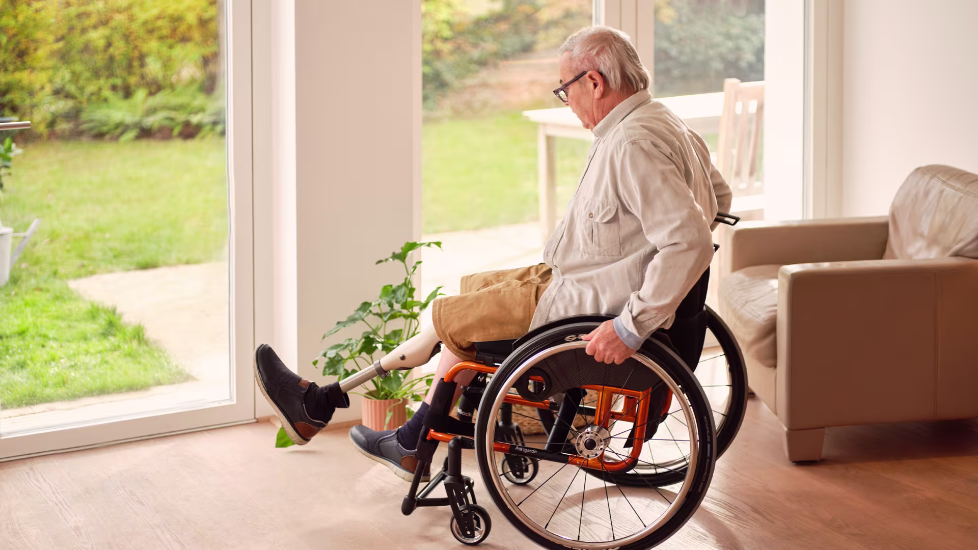 Ein älterer Mann fährt mit seinem Rollstuhl durch das Haus. Er trägt zudem das mechatronische Prothesenkniegelenk Kenevo von Ottobock.