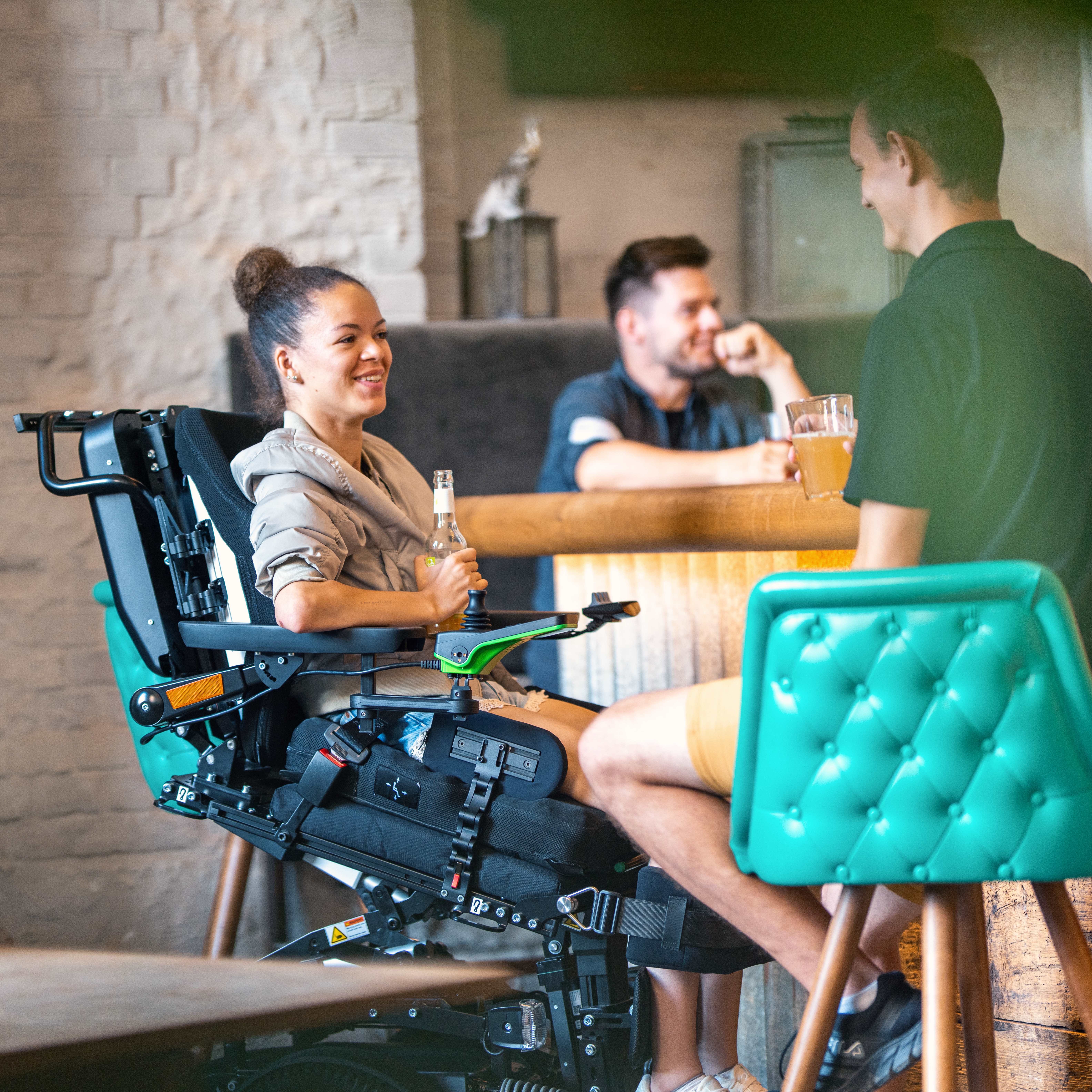 Juvo B7 user Elisa sitting in her Juvo B7 in a bar holding a beverage. 