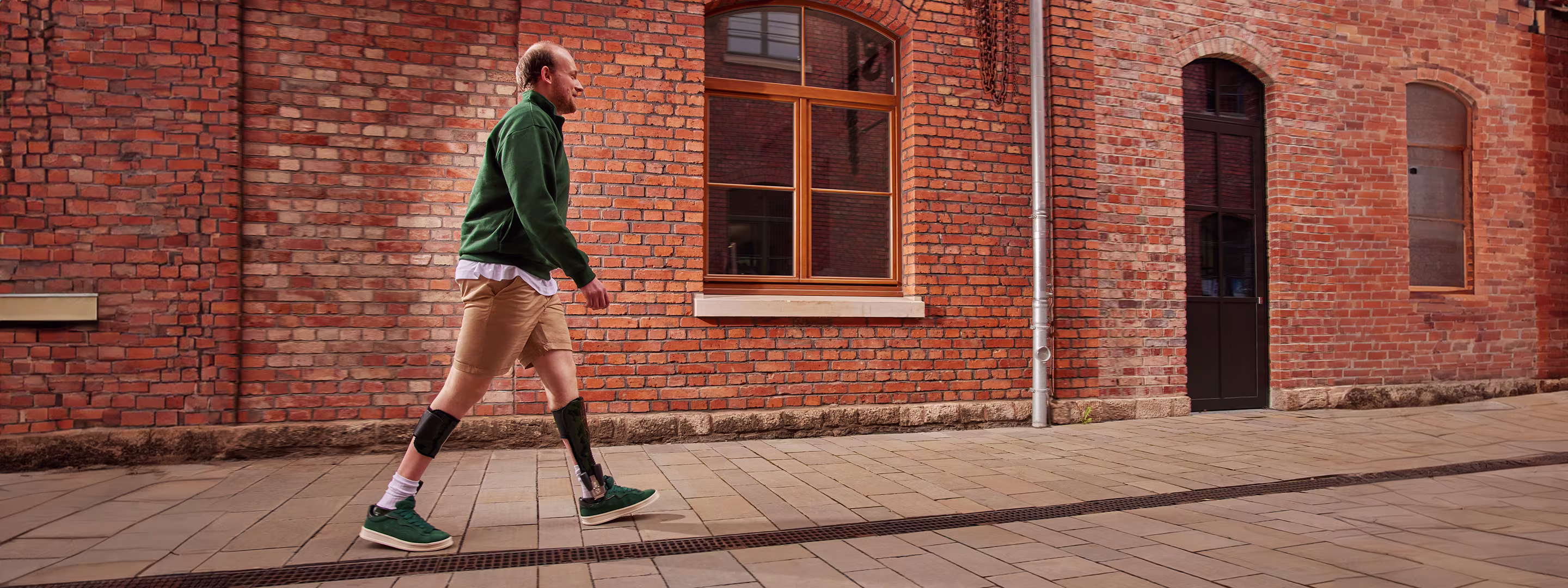 Man wearing ankle-foot-orthoses is walking in front of a brick wall.