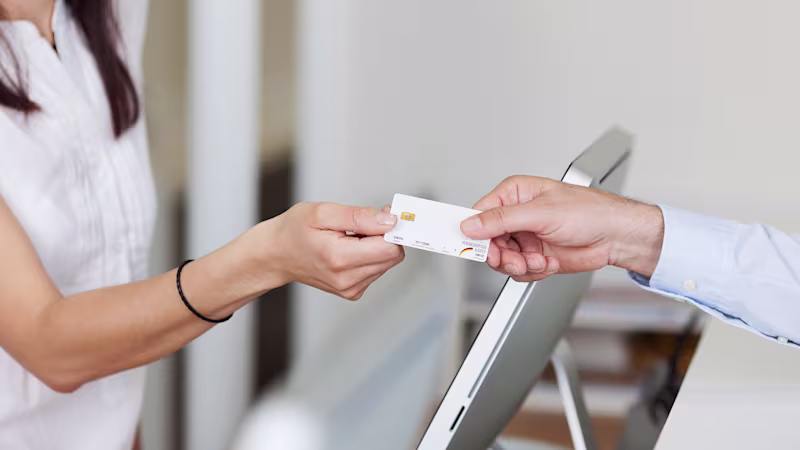 Female patient hands her insurance card to the receptionist at a medical clinic.