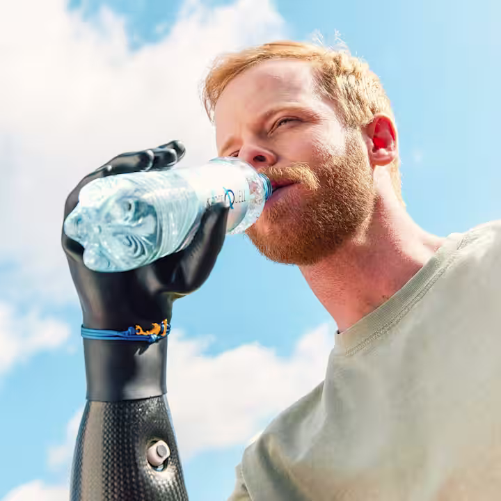 Ein Handprothesenträger trinkt aus einer Wasserflasche. Er trägt die Michelangelo Hand und bebionic Hand von Ottobock.
