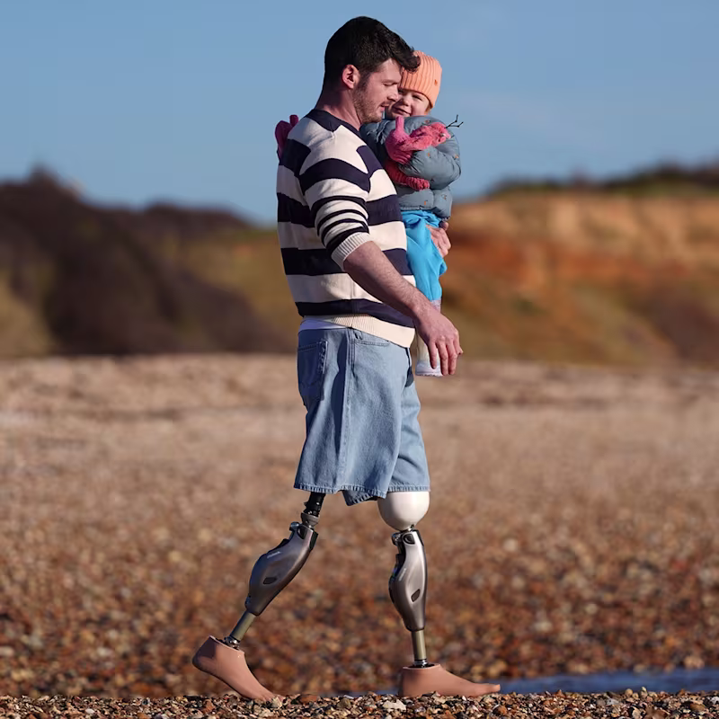 Mężczyzna, po amputacji obu nóg, idzie po plaży korzystając z nowoczesnych protez Genium X4