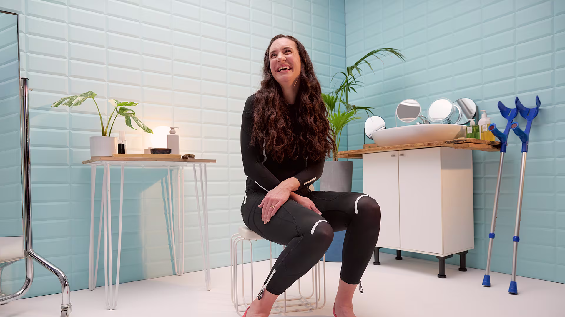 A smiling woman sits on a chair in a bathroom wearing the Ottobock exopulse suit