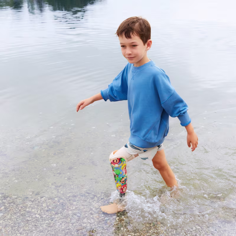 Auf dem Bild sieht man einen kleinen jungen der an einem Gewässer entlang läuft und die Beinprothese Maverick junior trägt.