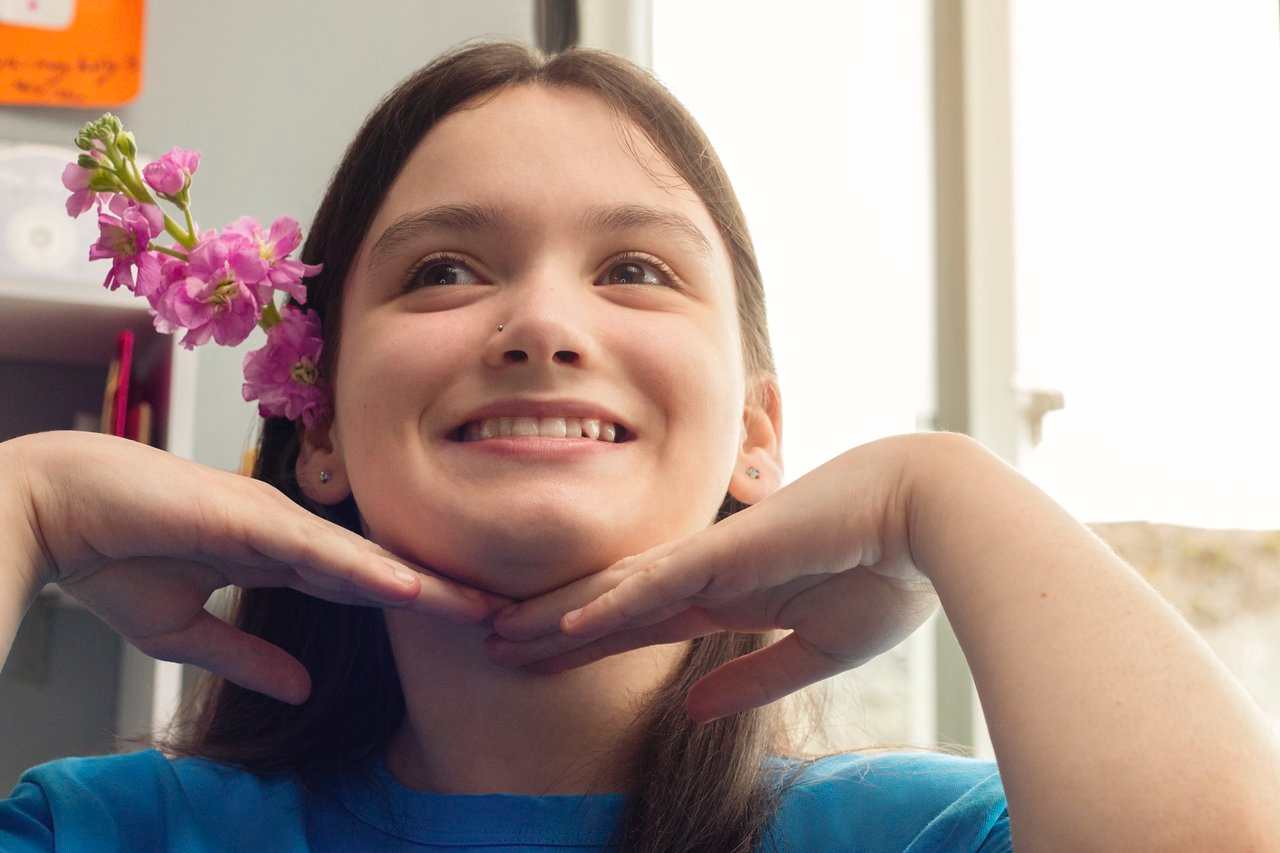 Ein junges Mädchen mit Zerebralparese hat eine Blume hinter dem Ohr und lächelt.