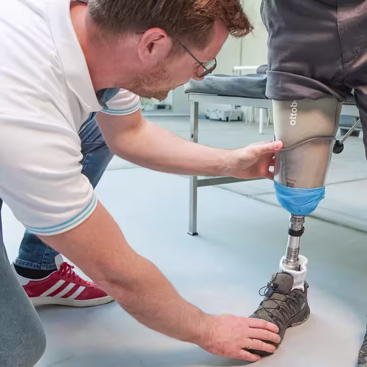 Ein Orthopädietechniker kniet auf dem Boden und justiert einen MyFit TT Schaft von Ottobock bei einem amputierten Mann.