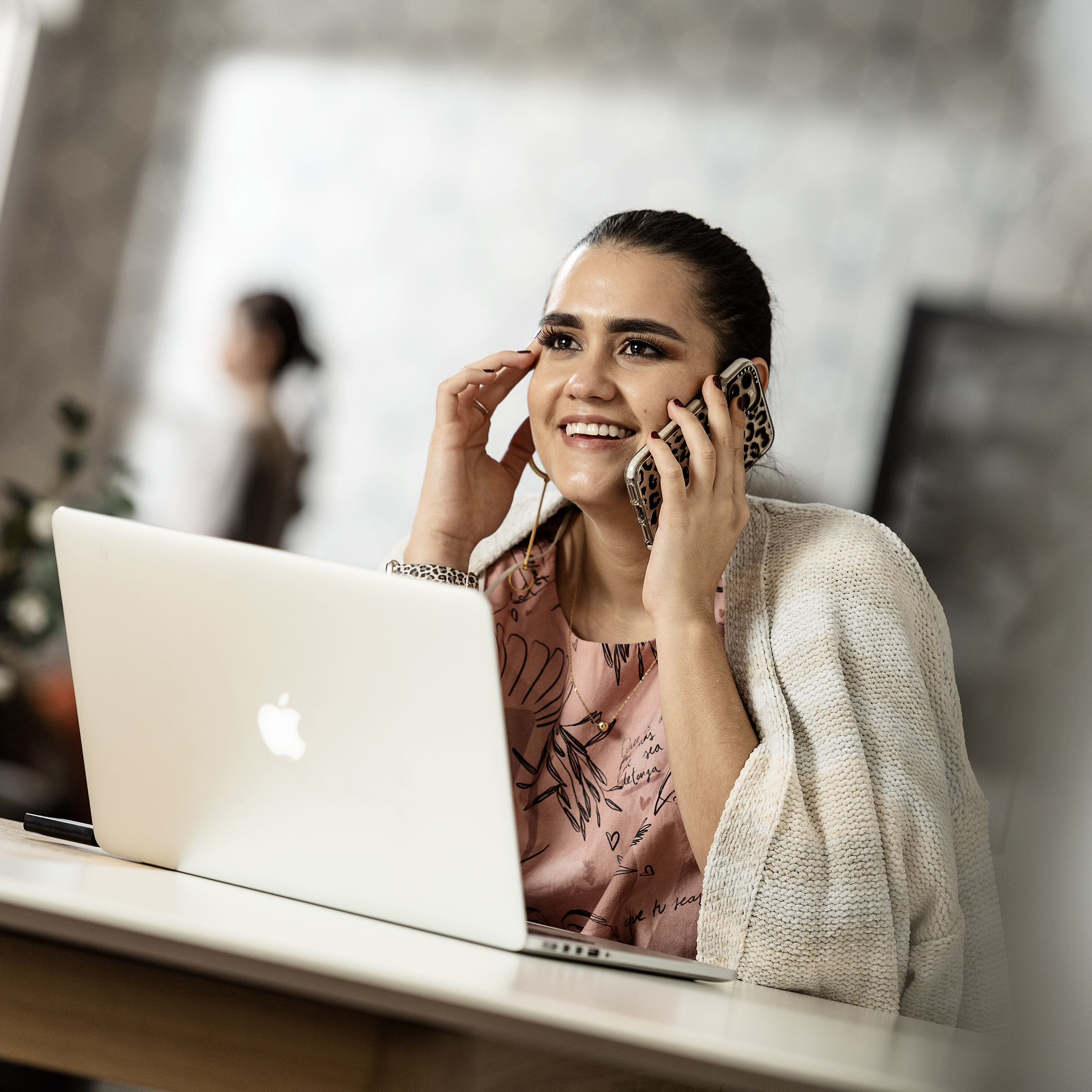 Woman working on her laptop while having a phone conversation in a professional environment.