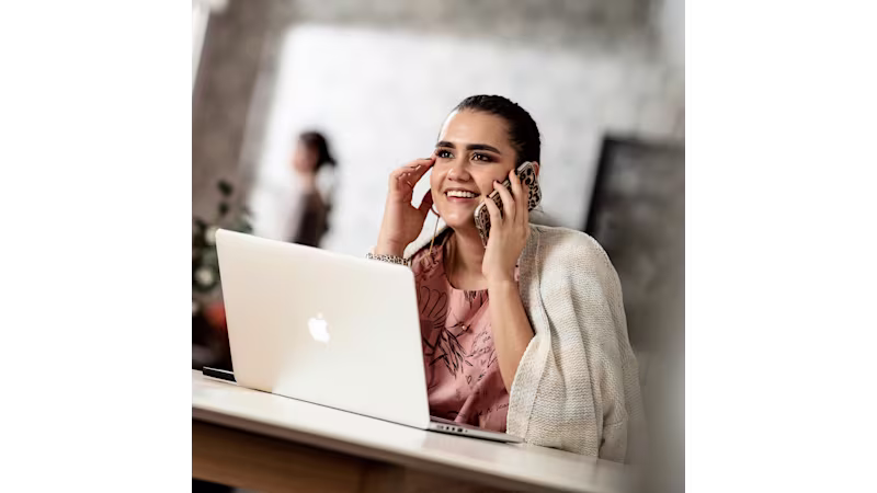 Woman working on her laptop while having a phone conversation in a professional environment.