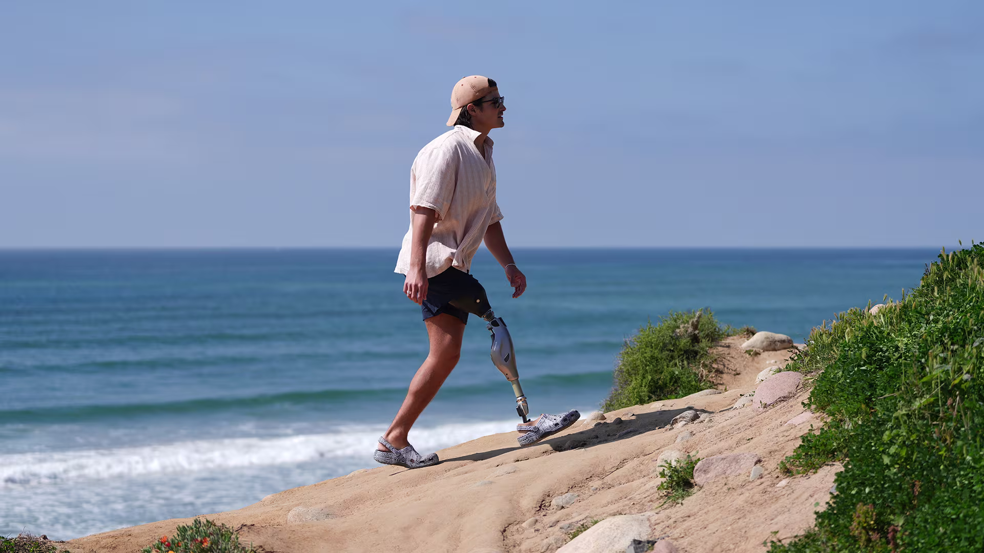 An amputee wearing his Ottobock Genium X4 while walking over a dune by the beach.