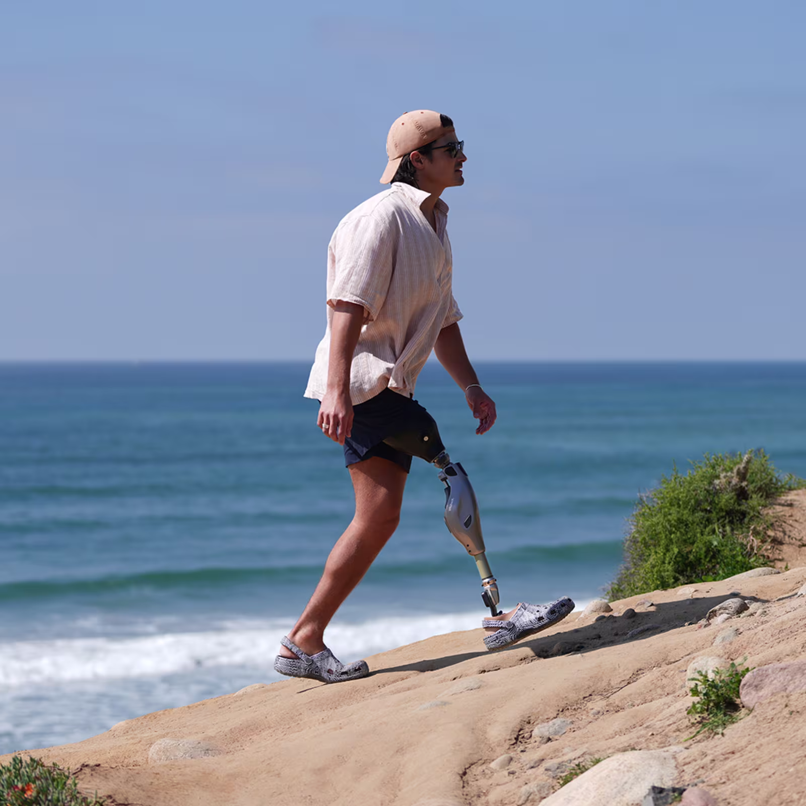 An amputee wearing his Ottobock Genium X4 while walking over a dune by the beach.