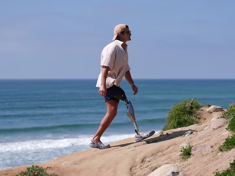 An amputee wearing his Ottobock Genium X4 while walking over a dune by the beach.
