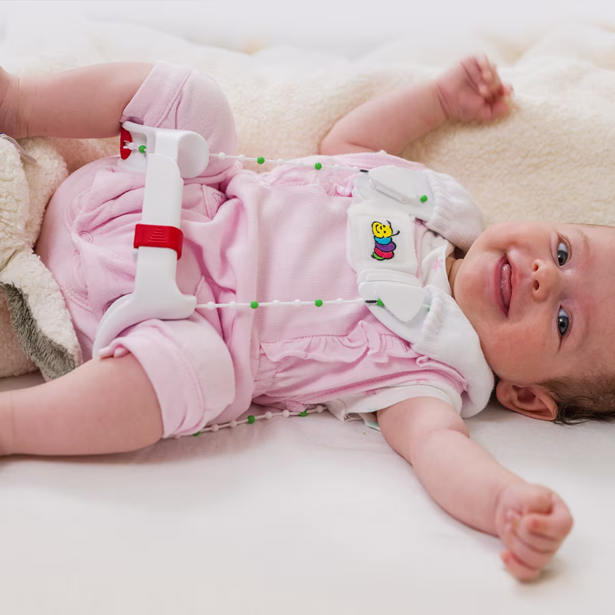 Ein Baby liegt auf einem Wickeltisch und lacht in die Kamera. Die Mutter zeiht dem Kind eine Tübinger Hüftbeugeschiene von Ottobock an.