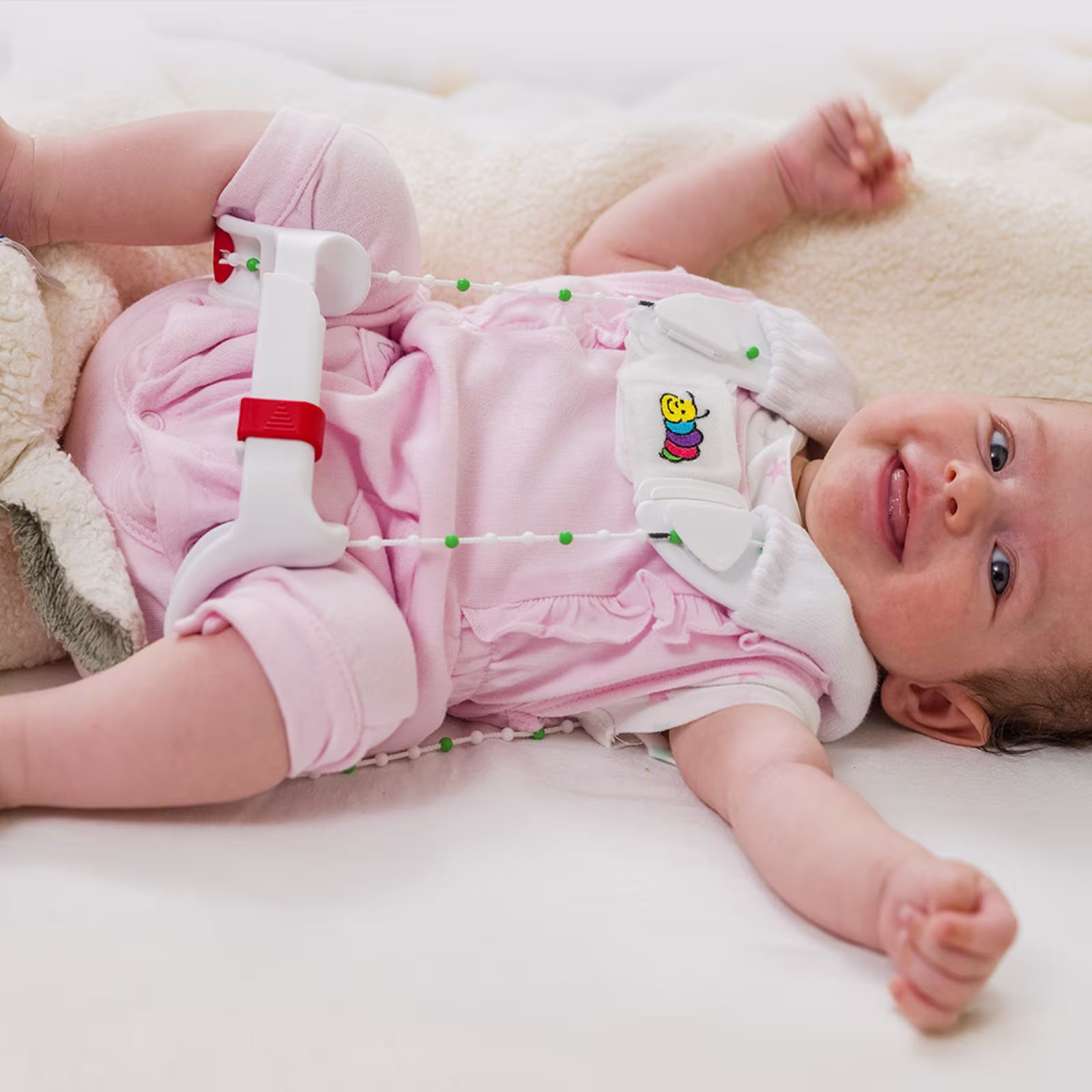 Ein Baby liegt auf einem Wickeltisch und lacht in die Kamera. Die Mutter zeiht dem Kind eine Tübinger Hüftbeugeschiene von Ottobock an.