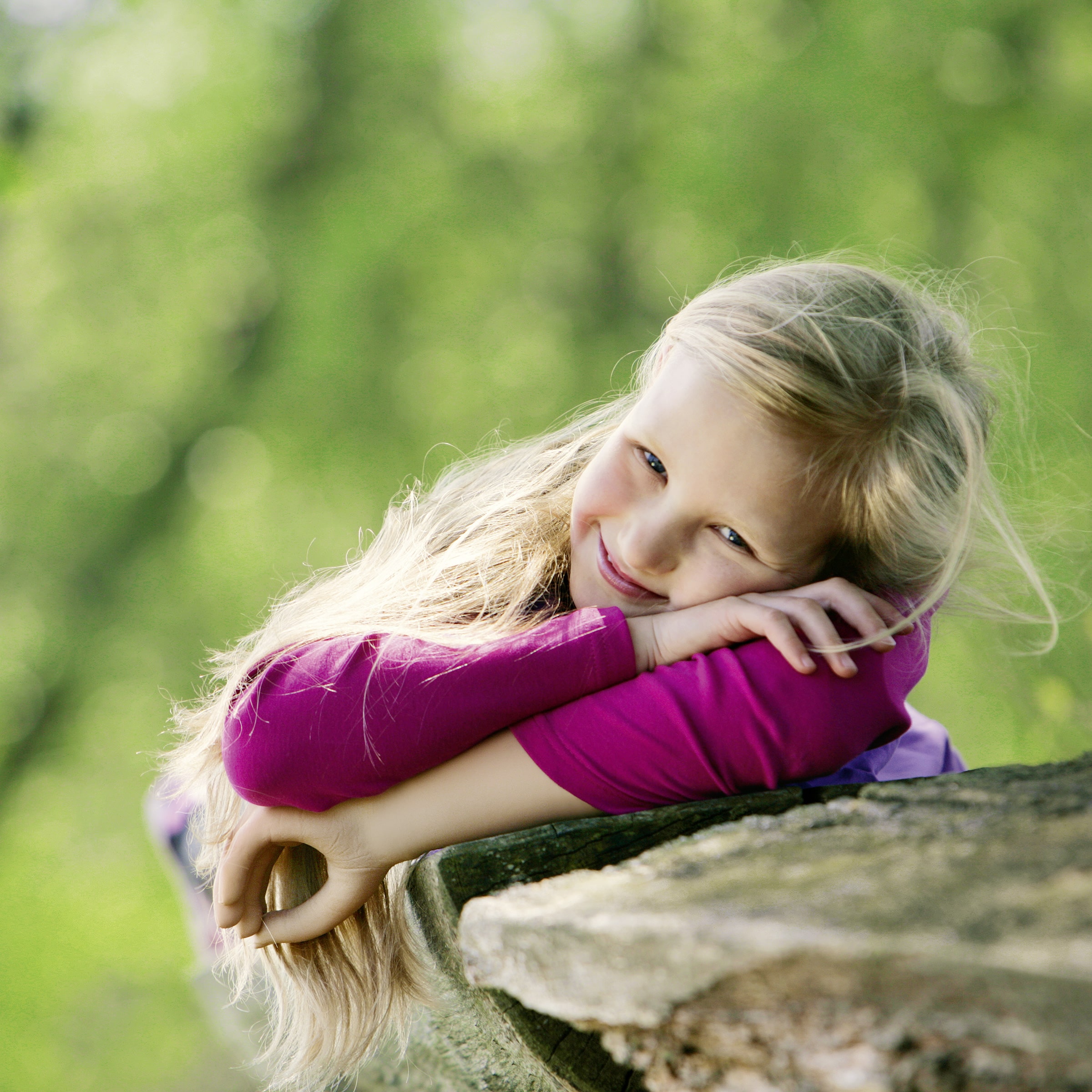 A young girl with an Electric Hand 2000 prosthetic hand from Ottobock resting with folding arms on a tree branch.