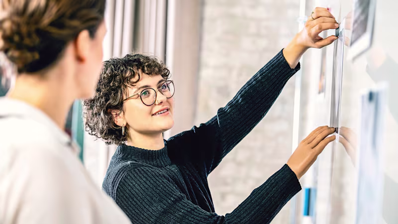 Eine Armprothesenträgerin steht vor einem Whiteboard im Büro und erklärt etwas Ihrem Kollegen. Sie trägt Myoelektrischen Armprothese mit der Myo Plus Mustererkennung von Ottobock.