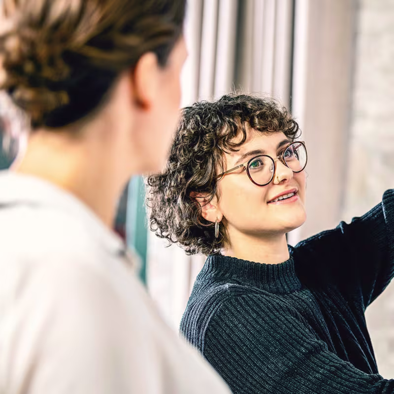 Eine Armprothesenträgerin steht vor einem Whiteboard im Büro und erklärt etwas Ihrem Kollegen. Sie trägt Myoelektrischen Armprothese mit der Myo Plus Mustererkennung von Ottobock.