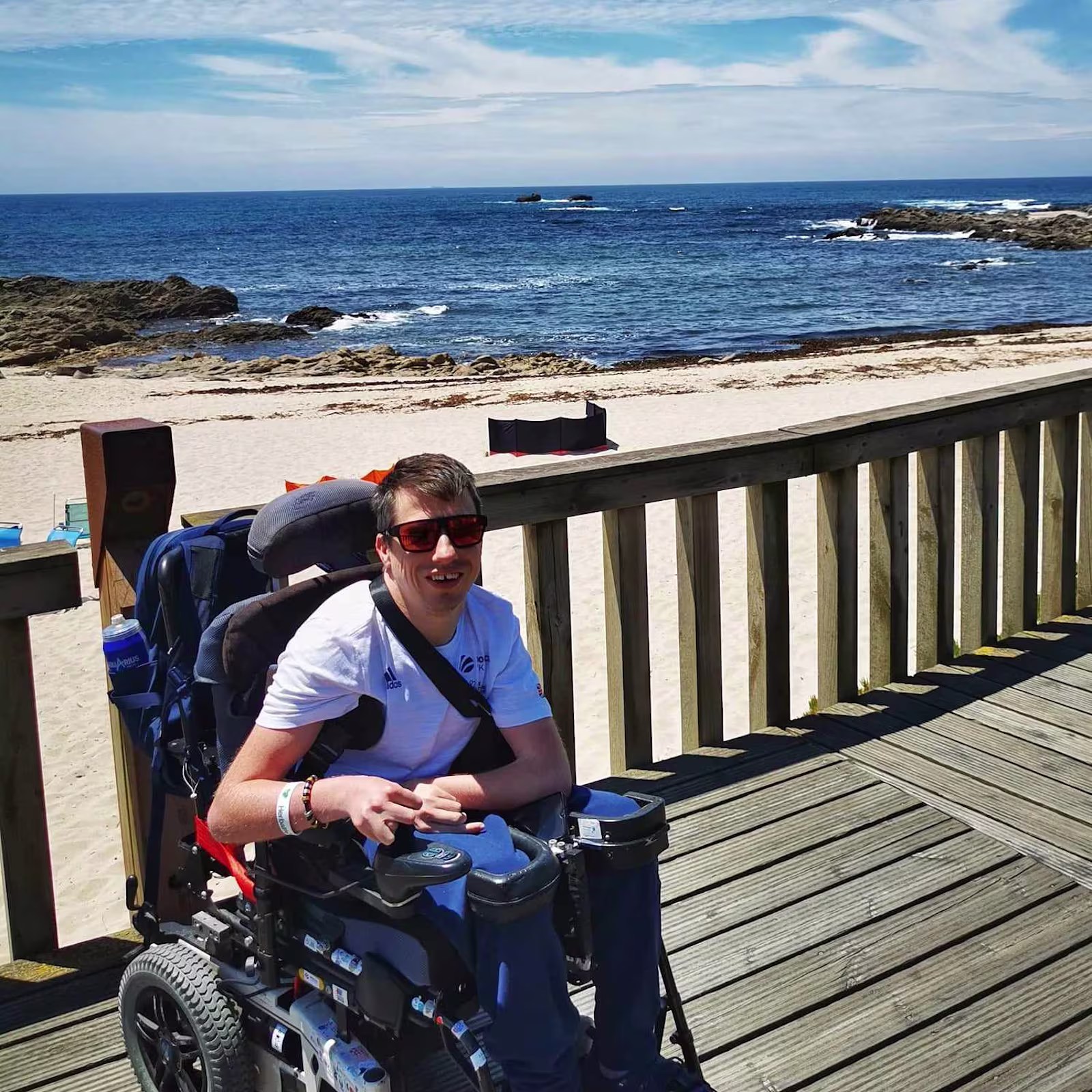David Smith OBE sits in his B400 wheelchair from Ottobock on a deck with a beach behind him.