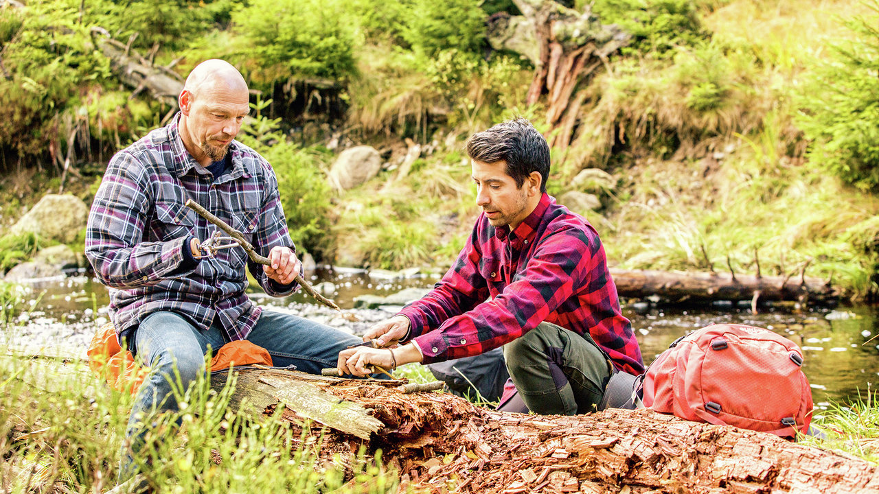 Ein Armprothesenträger sitzt im Wald auf einem Baumstumpf und schneidet mit einem anderen Mann Holz klein. Er trägt Holgers das DynamicArm-Ellbogengelenk mit der VariPlus Speed Hand von Ottobock.