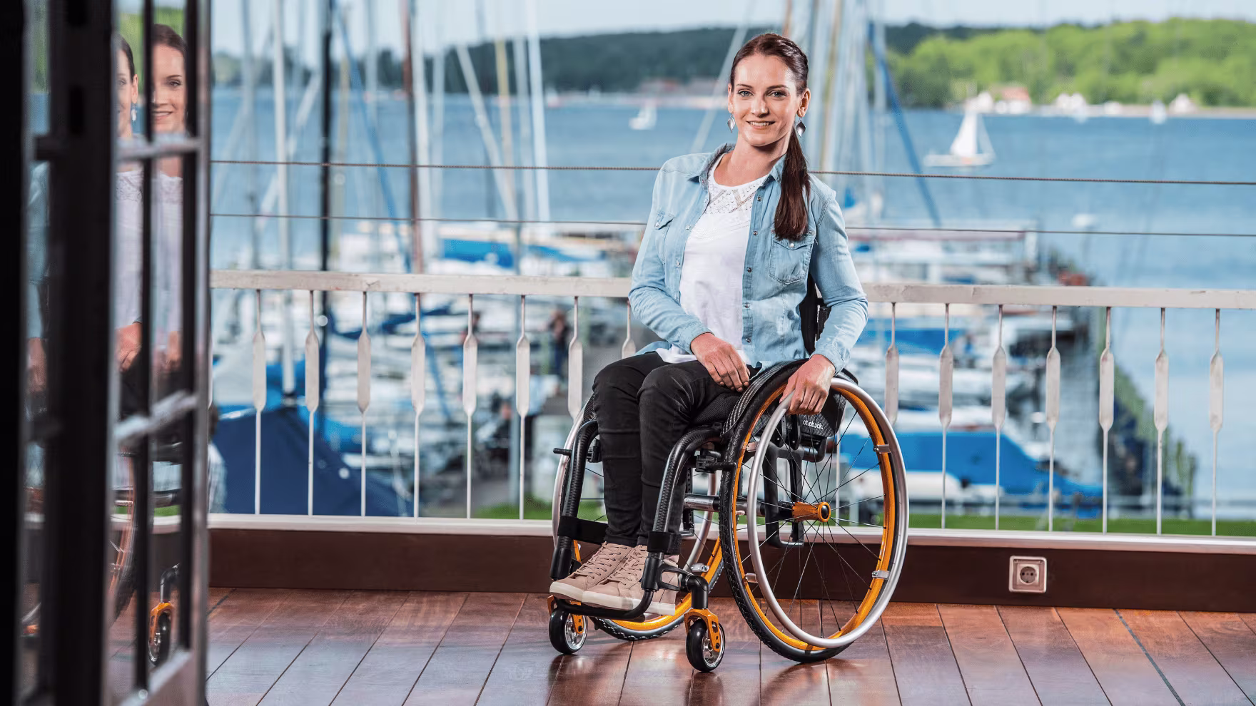 A lady in her Zenit R CLT lightweight manual wheelchair from Ottobock sitting in front of a lake with boats moored. 