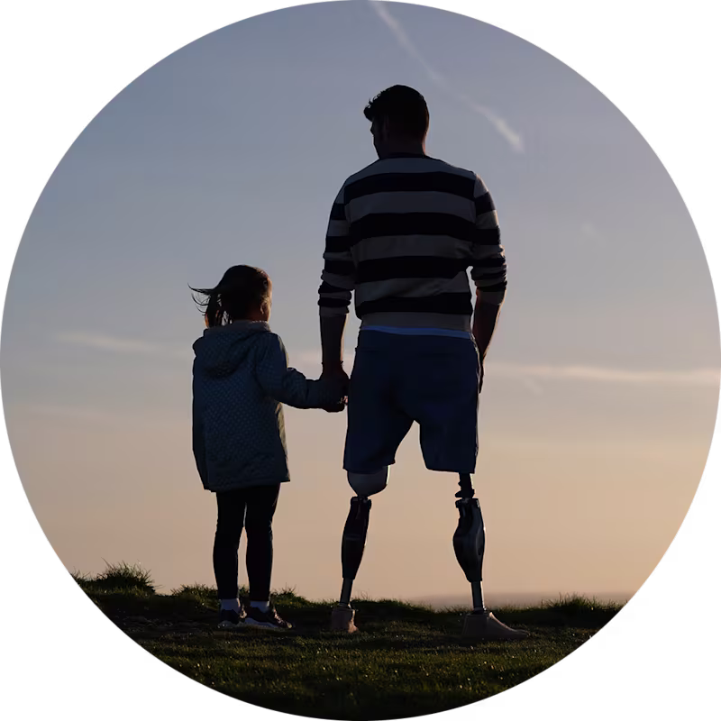 Veteran and bilateral Genium X4 Prosthetic Knee user Dave Henson standing with his daughter by a cliff edge with a sunset backdrop