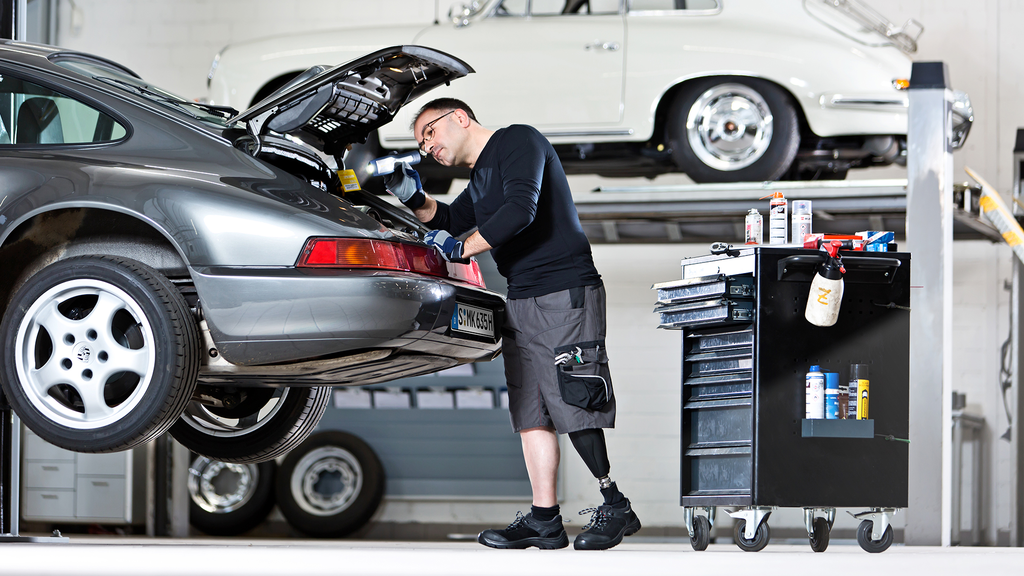 A person with a transfemoral amputation repairs a car in a workshop setting.