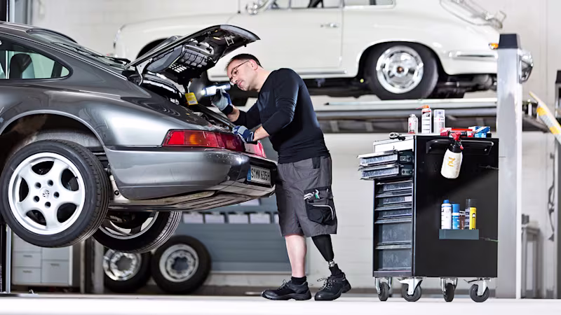 A person with a transfemoral amputation repairs a car in a workshop setting.