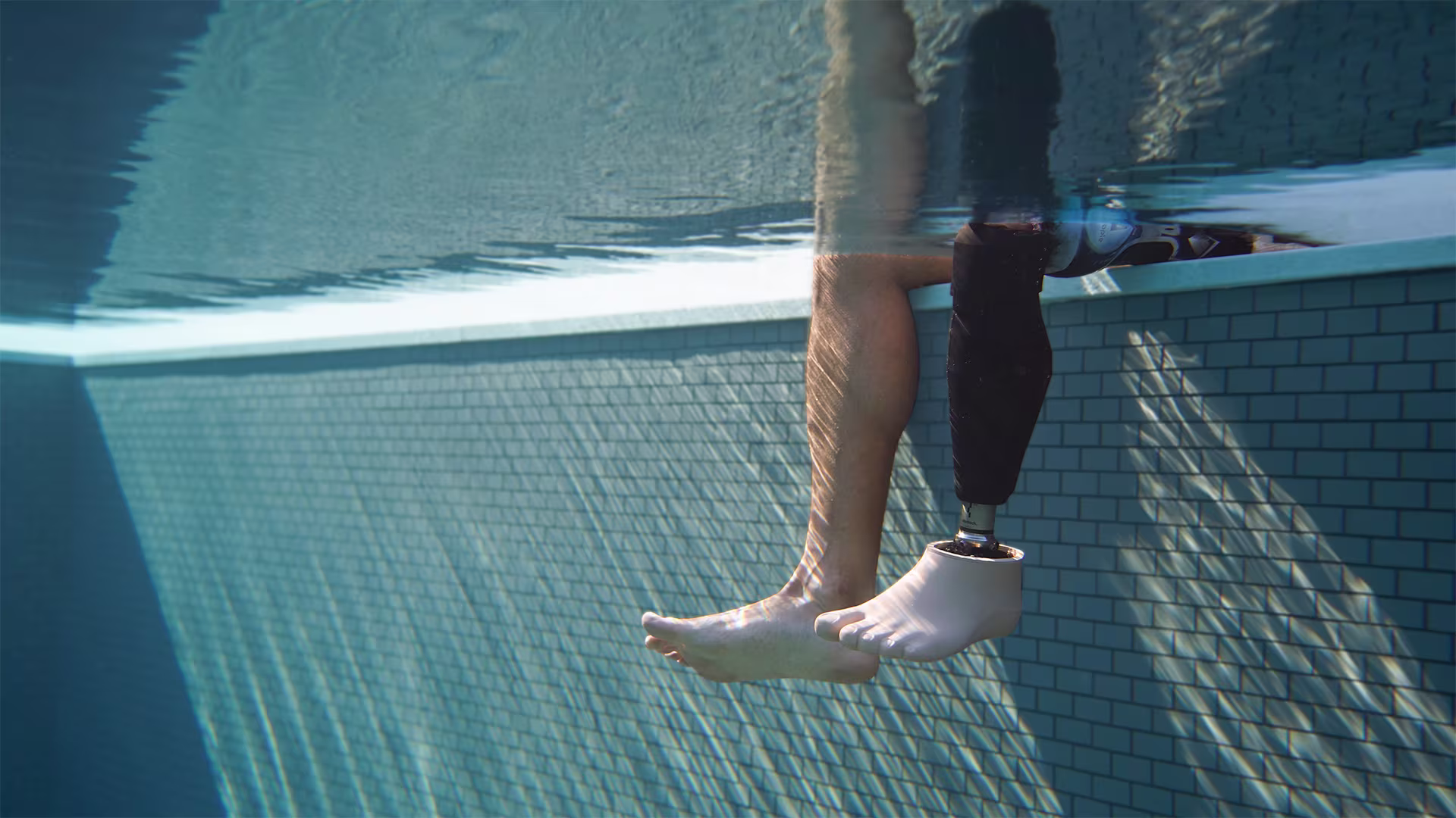 An underwater photo in a swimming pool of an Ottobock Evanto prosthetic foot and Genium X3 microprocessor knee and a natural leg.