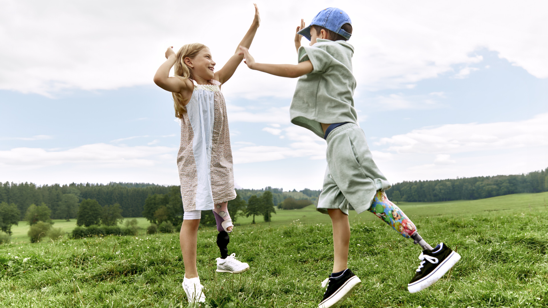 Auf dem Bild sieht man zwei Kinder, einen Jungen und ein Mädchen. Beide springen hoch und klatschen sich in der Luft zu. Das Mädchen trägt das Movido Kniegelenk mit dem Maverick junior Prothesenfuß und der Junge trägt den Maverick junior Prothesenfuß.