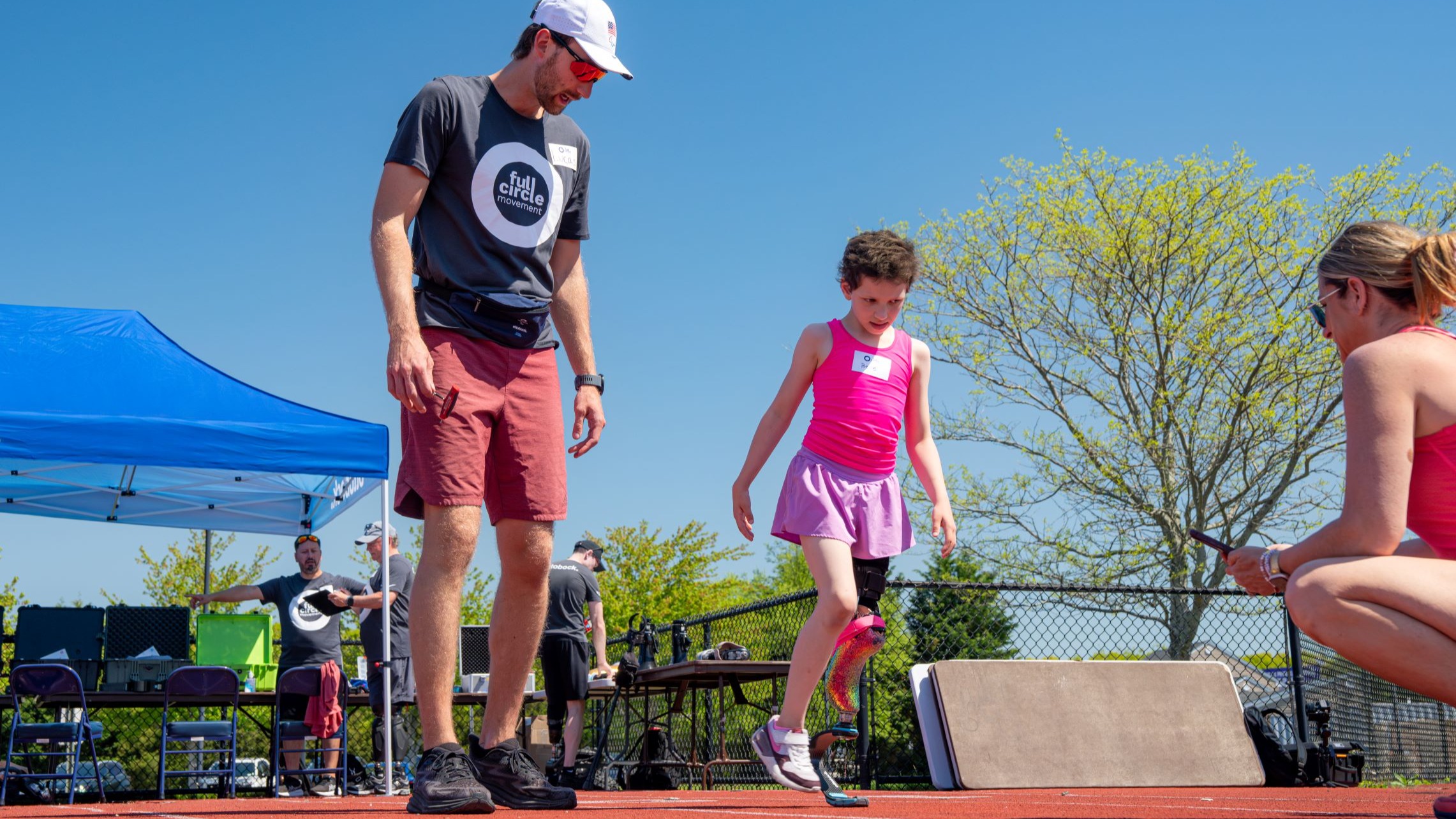Running coach, Lucas Crisanti, observes girl taking first steps in running blade prosthetic leg