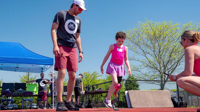 Running coach, Lucas Crisanti, observes girl taking first steps in running blade prosthetic leg