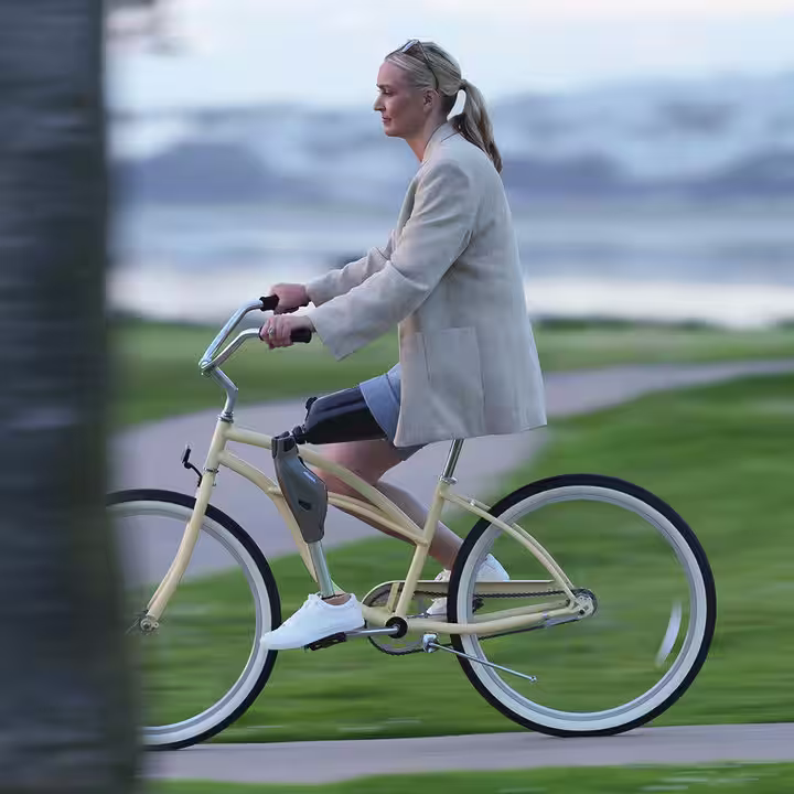 Eine weiblich gelesene Prothesenträgerin fährt mit einem gelben Fahrrad durch die Natur. Sie trägt dabei das mechatronische Prothesenkniegelenk Genium X4 von Ottobock.