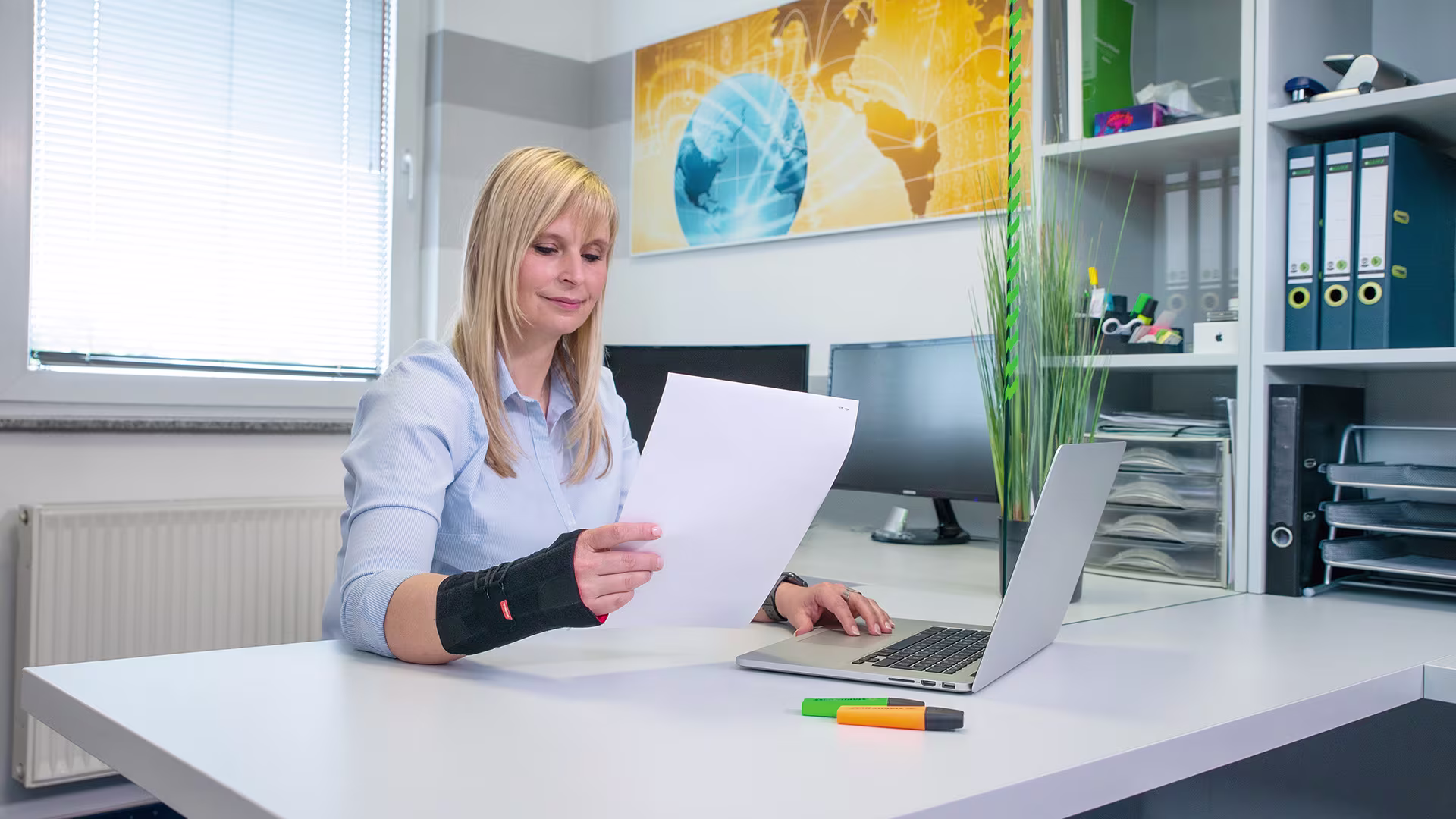 A woman in an office wears an Ottobock hand brace while reviewing her work on a piece of paper 