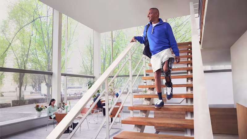 Ein Mann mit der Beinorthese C-Brace von Ottobock geht eine Treppe herunter und lächelt dabei.