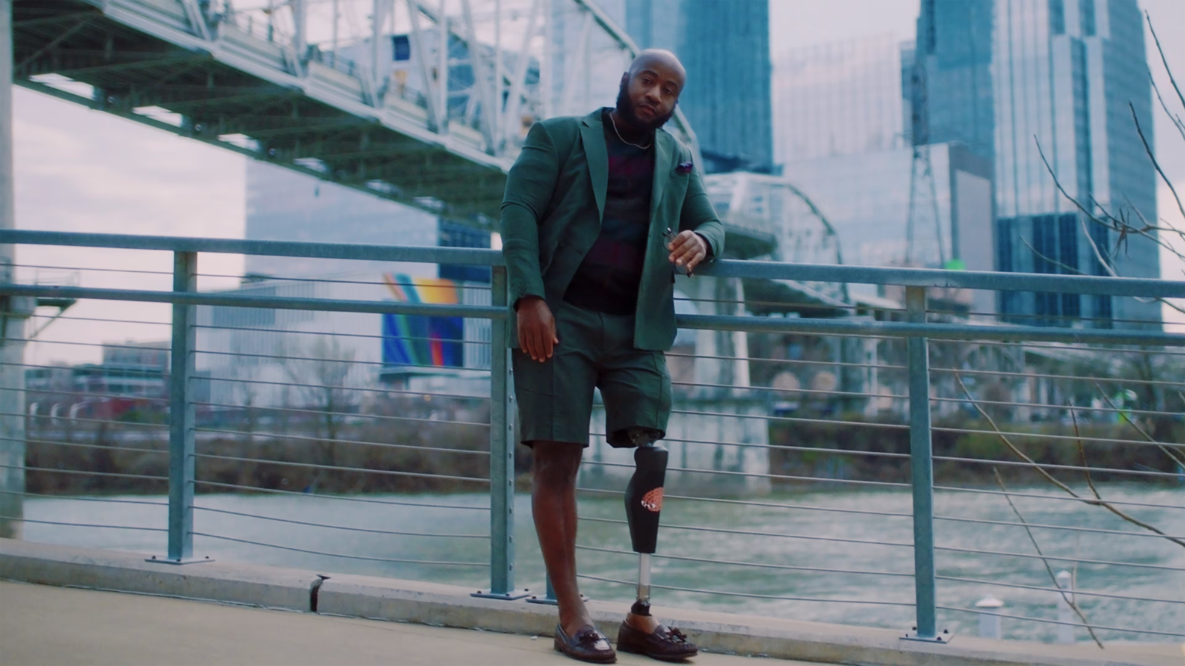 In his C-Leg 4, Brandon leans on a rail overlooking water and the city
