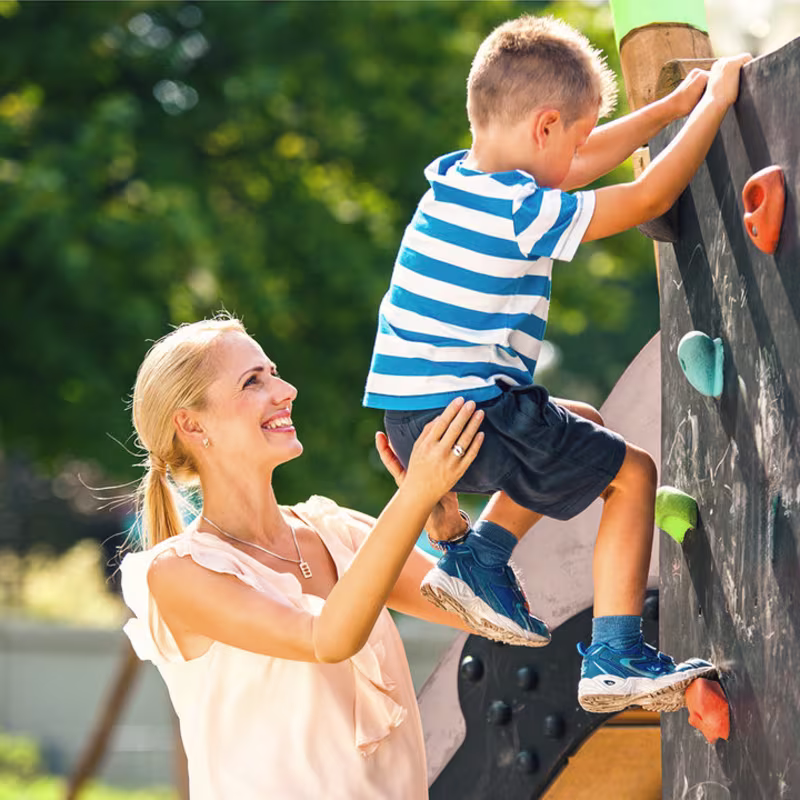 Eine Armprothesenträgerin spielt mit Ihrem Kind auf einem Spielplatz. Sie trägt die MyoHand VariPlus Speed von Ottobock.
