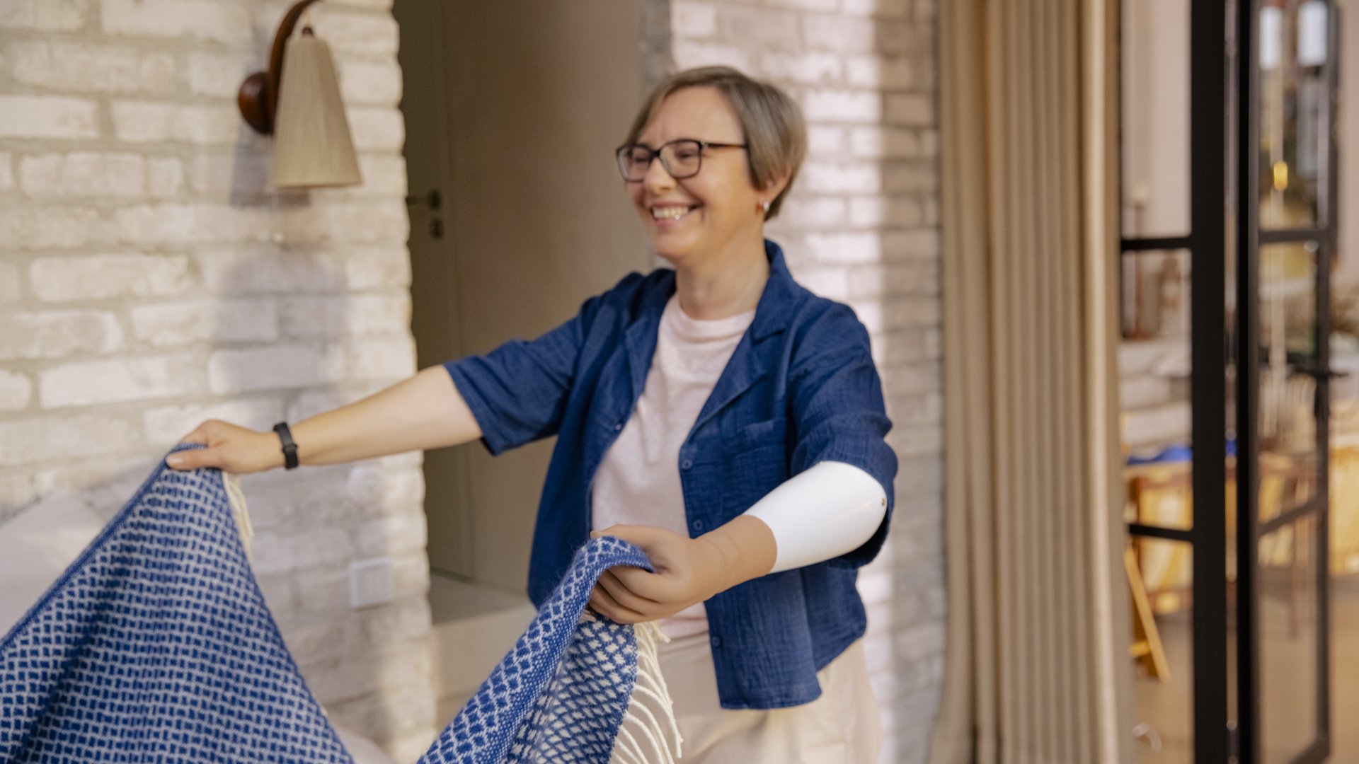 Ottobock female prosthetic hand user folding a bed cover at home.