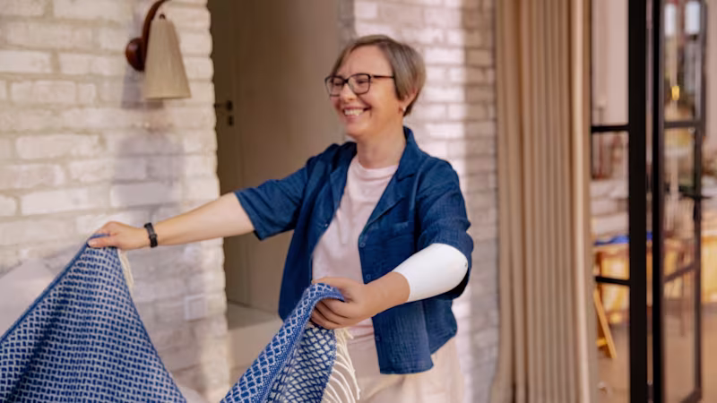 Ottobock female prosthetic hand user folding a bed cover at home.