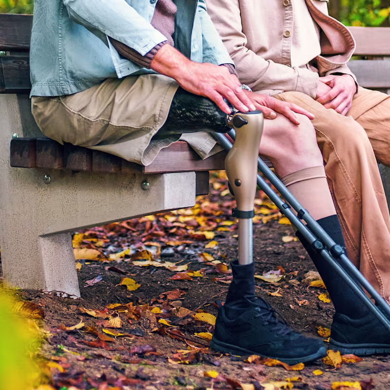 2 people sitting on a park bench, one person wearing an Ottobock Kenevo microprocessor knee