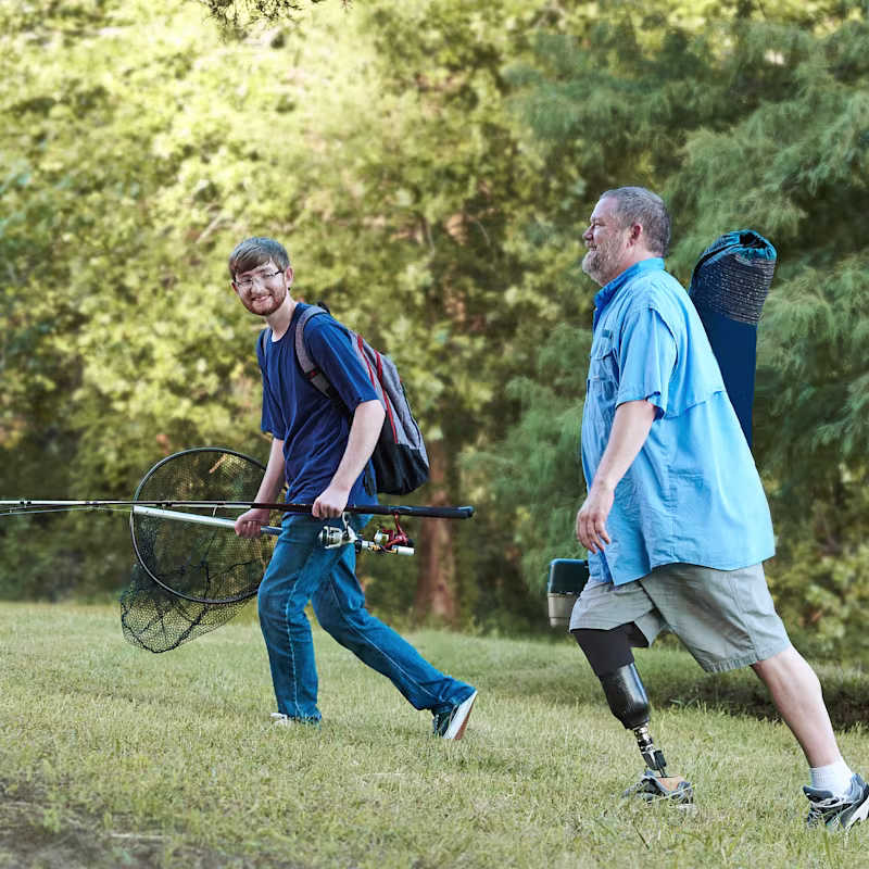 Vater und Sohn gehen mit ihrer Angelausrütung einen begrasten Hügel hinauf.