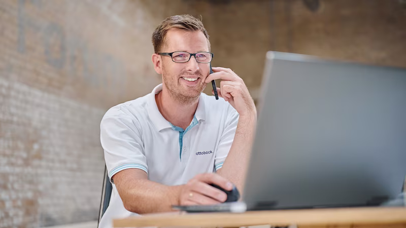 Ein Mitarbeiter von Ottobock, eine männlich gelesene Person, sitzt im Büro am Computer und telefoniert.