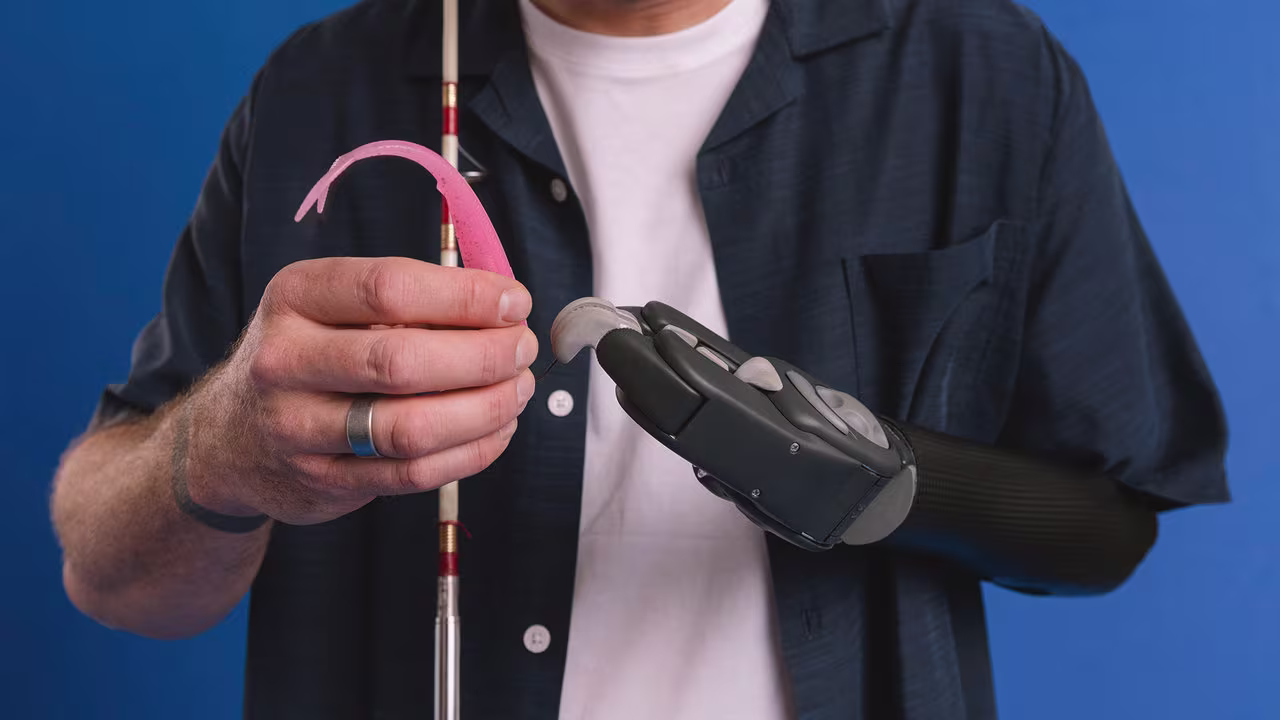 Ein Prothesenträger hält eine Angeln mit einem Angelhaken in der Hand. Er trägt die Michelangelo Hand und bebionic Hand von Ottobock.
