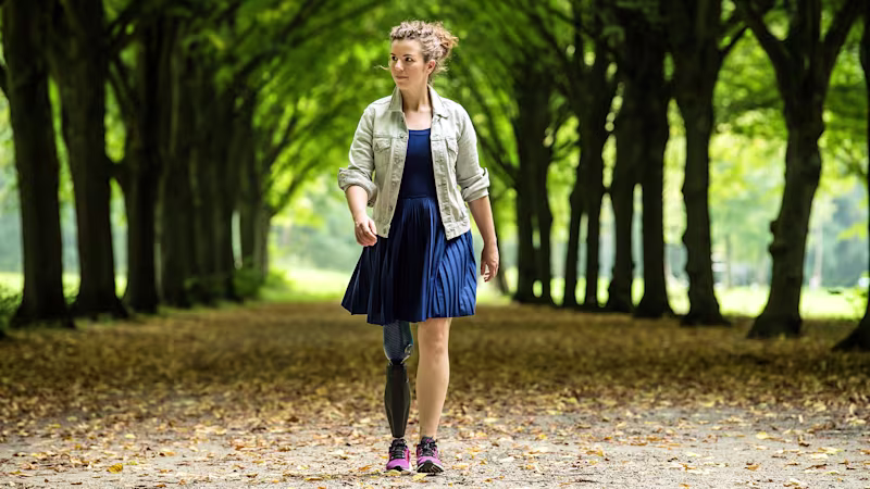 Eine weiblich gelesene Prothesenträgerin geht spazieren. Im Hintergrund ist eine Allee aus Bäumen.