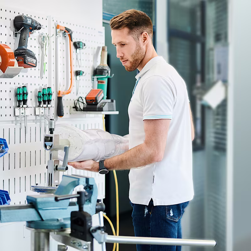 Orthopädietechniker hält ein Gipsmodell in einer O&P-Werkstatt vor einem Arbeitsplatz.